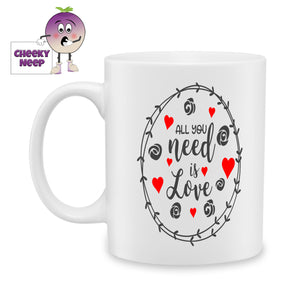 White ceramic mug with "All you need is love" printed on the mug surrounded by love hearts in red and pictures of rose buds and a wreath in black as produced by Cheekyneep.com