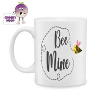 White ceramic mug with a large bumble bee with a heart shaped pink wing and the words Bee mine on the mug as produced by Cheekyneep.com