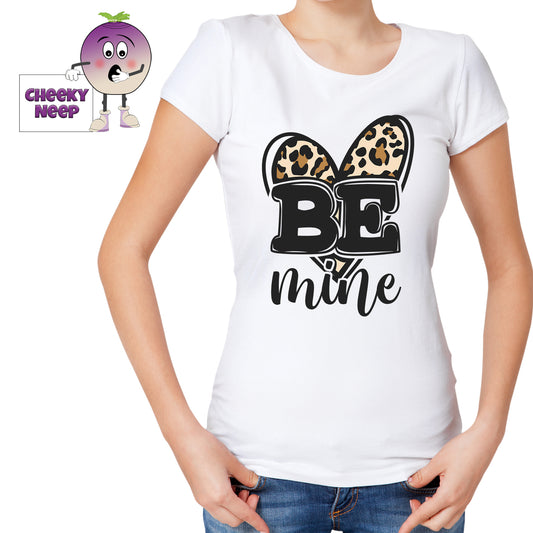 Woman in a white tee with the slogan "Be Mine" printed in front of a leopard print heart shape on the tee. Tee as produced by Cheekyneep.com