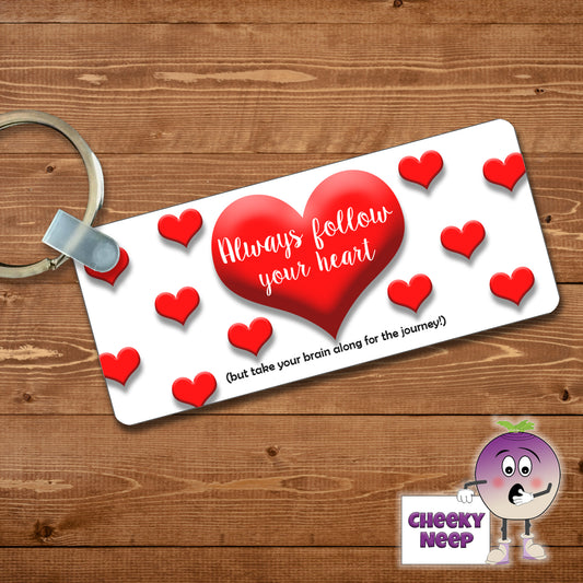 Rectangular plastic keyring with the words "Always follow your heart" printed in white over a large red heart surrounded by other smaller red hearts. Below the main heart is the words "(but take your brain along for the journey)" printed in black. The keyring is printed on both sides.