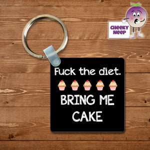 Black square keyring with the words "Fuck the diet. Bring me cake"  and five pictures of mini cakes printed on the keyring as supplied by Cheekyneep.com