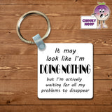 Square plastic keyring with the words "It may look like I'm DOING NOTHING but I'm actively waiting for all my problems to disappear" printed on both sides.