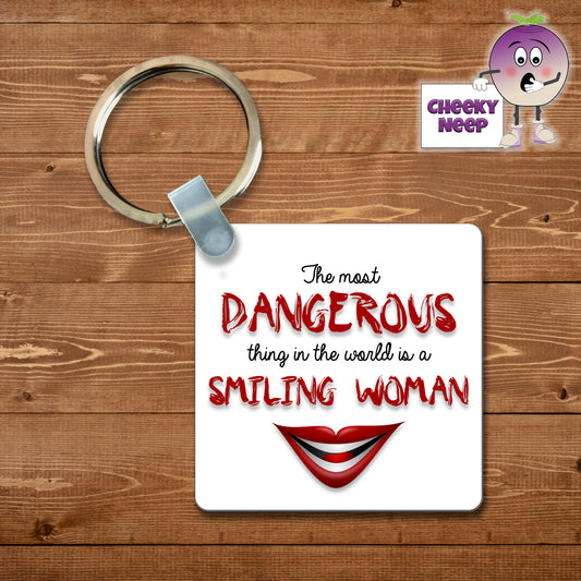 Square plastic keyring with the words "The most dangerous thing in the world is a smiling woman" printed on both sides together with a cartoon smiling mouth.