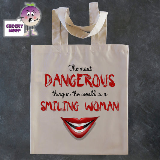 Tote Shopping bag in natural with the words "The most DANGEROUS thing in the world is a SMILING WOMAN" printed on the bag